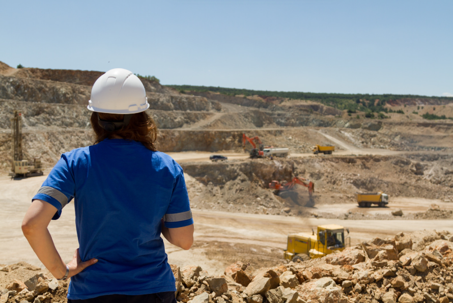 Woman in a blue shirt and white hard hat looks over a mining site.