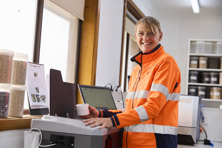 Woman in an orange work vest in an office environment smiles at the camera